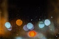 An abstract background of night street lights bokeh through wet glass, close-up with selective focus Royalty Free Stock Photo