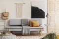 Abstract black and white painting and handmade macrame on white wall of natural living room interior with grey fashionable couch