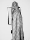 Abstract black and white shot of a person covered in a blanket in front of an artwork frame