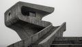 An abstract brutalist structure featuring a large, curved concrete form with a staircase leading to a squared observation platform