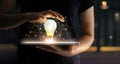 Human hands holding light bulb glowing on tablet network Royalty Free Stock Photo