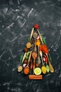 Abstract Christmas tree made of spices and seasoning in spoons. Black stone background. Top view, flat lay, vertical