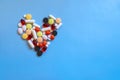 Abstract closeup of colorful heap of pills in heart shape on blue background.