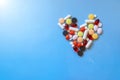 Abstract closeup of colorful heap of pills in heart shape on blue background.