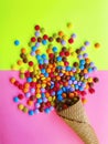 Multicolored small candies sprinkled from a waffle horn on a bright two-color background. Candy In Ice Cream Cone.