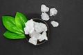 Abstract composition of green leaves, wooden dark bowl and big sugar or salt crystals on grey background with copy space