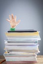 Abstract concept image showing a young student behind a large pile of test prep books on a study desk