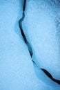An abstract detailed vertical close up photograph of a crack or fault line in the blue frozen ice layer on a lake