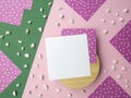 Square note sheet on wooden base,pink green paper,corner of lilac paper white polka dots on perimeter,pebbles,copy space