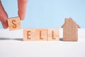 Abstract house made of cardboard hand holds with wooden cubes with the word sell. Home sale concept Royalty Free Stock Photo