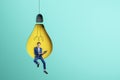 Abstract image of attractive young european businessman sitting on abstract hanging light bulb chair and using laptop on blue Royalty Free Stock Photo