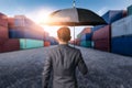 The abstract image of the Businessman is spreading umbrella during sunrise overlay with container yard image. The concept of trans