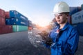 The abstract image of engineer point to the hologram on his smartphone and blurred container yard is backdrop.