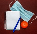 Abstract image with medical mask, tangerine, pen and notepad with blank lettering Royalty Free Stock Photo