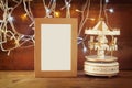 Abstract image of old vintage white carousel horses with garland gold lights and blank frame on wooden table. retro filtered image Royalty Free Stock Photo