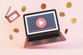 Abstract image of paid online movie theater concept with laptop and dollar coins on pink background.