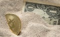 Bitcoin currency seen partially buried in Silicon Sand together with a One Dollar Banknote. Royalty Free Stock Photo