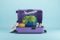 Abstract image of suitcase filled with airplane, globe and beach items on blue background. Summer vacation, tour agency and travel Royalty Free Stock Photo