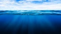 Tropical underwater dark blue deep ocean wide nature background with rays of sunlight and blue sky in background.