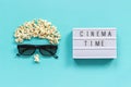 Abstract image of viewer, 3D glasses, popcorn and light box text Cinema time on blue paper background. Concept cinema movie and Royalty Free Stock Photo