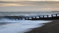 Abstract long exposure landscape image of waves crashing onto groynes on beach during sunset