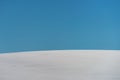 Abstract minimalistic winter landscape, snow covered hill with blue sky in background on sunny day