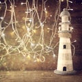 Abstract nautical lifestyle concept. old vintage lighthouse on wooden table and warm gold garland lights. vintage filtered image