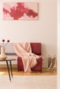 Abstract painting on the empty white wall of elegant living room with grey couch with pastel pink and burgundy blankets