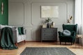 Abstract painting on grey wall o contemporary living room interior with emerald green armchair with round pillow, commode and Royalty Free Stock Photo