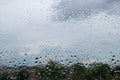 Abstract pattern consisting of random raindrops hanging on window after recent rain with background of blurred foliage and sky