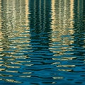 Abstract pattern of rippling water reflecting vertical structures, casting yellow and blue hues. Royalty Free Stock Photo