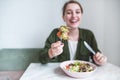 Abstract photo of a woman sitting at the table eating salad and sending herbs on the fork to the camera