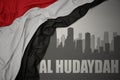 Abstract silhouette of the city with text Al Hudaydah near waving national flag of yemen on a gray background Royalty Free Stock Photo