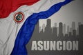 Abstract silhouette of the city with text asuncion near waving national flag of paraguay on a gray background