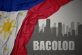 Abstract silhouette of the city with text Bacolod near waving national flag of philippines on a gray background.3D illustration