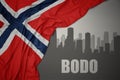 Abstract silhouette of the city with text Bodo near waving national flag of norway on a gray background