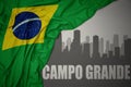 Abstract silhouette of the city with text Campo Grande near waving national flag of brazil on a gray background