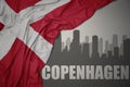 Abstract silhouette of the city with text Copenhagen near waving national flag of denmark on a gray background