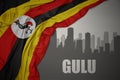 Abstract silhouette of the city with text Gulu near waving colorful national flag of uganda on a gray background