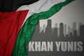 Abstract silhouette of the city with text Khan Yunis near waving national flag of palestine on a gray background.3D illustration Royalty Free Stock Photo