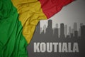 Abstract silhouette of the city with text Koutiala near waving colorful national flag of mali on a gray background