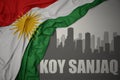 Abstract silhouette of the city with text Koy Sanjaq near waving national flag of kurdistan on a gray background.3D illustration