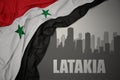 Abstract silhouette of the city with text Latakia near waving national flag of syria on a gray background