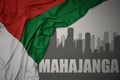 Abstract silhouette of the city with text Mahajanga near waving colorful national flag of madagascar on a gray background Royalty Free Stock Photo