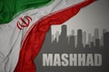 Abstract silhouette of the city with text Mashhad near waving national flag of iran on a gray background.3D illustration