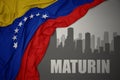 Abstract silhouette of the city with text Maturin near waving national flag of venezuela on a gray background