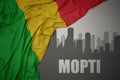 Abstract silhouette of the city with text Mopti near waving colorful national flag of mali on a gray background