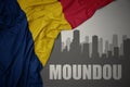 Abstract silhouette of the city with text Moundou near waving colorful national flag of chad on a gray background