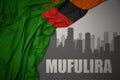 Abstract silhouette of the city with text Mufulira near waving colorful national flag of zambia on a gray background Royalty Free Stock Photo