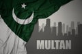 Abstract silhouette of the city with text Multan near waving national flag of pakistan on a gray background.3D illustration